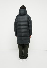 Abrigo tipo plumón en gris oscuro con cintura ajustada, capucha y diseño acolchado horizontal. Con longitud extendida y textura suave.