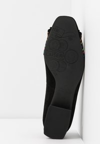 Semelle de chaussure en daim noir avec détails gravés, dotée d'un talon plat en caoutchouc texturé. Accents de bandes colorées au bord du talon.