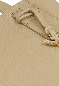 Beżowa skórzana torba z fakturowaną powierzchnią, cienkim paskiem i akcentami w odcieniu złota. Zbliżenie ukazuje detale szycia.