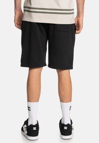 Zwarte shorts met een ontspannen pasvorm, van katoen, midden-dijlengte en een enkele achterzak. Draagt witte sokken tot de knie en zwarte sneakers.