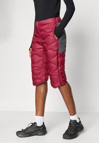 Μπορντό κοντά παντελόνια με γκρι πλευρικές πάνες. Διαθέτουν υφή στην επιφάνεια και πλαϊνές τσέπες, συνδυασμένα με μαύρα παπούτσια πεζοπορίας και λευκές κάλτσες.