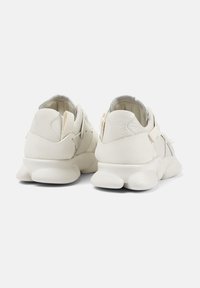 White sneakers with a textured leather upper, soft fabric lining, and chunky foam sole. Features minimalistic design and adjustable laces.