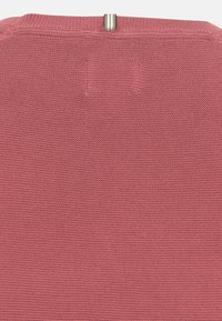 Gros plan d’un tissu tricoté rose avec une petite boucle en tissu grise et blanche au centre en haut.