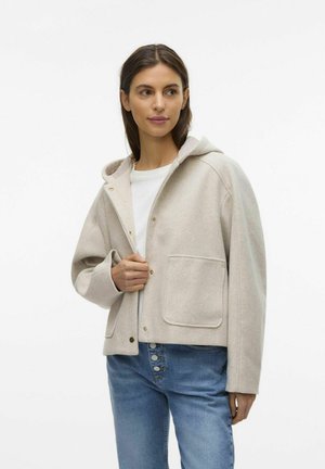 Ljus beige huvjacka gjord av mjukt tyg, med guldknappar, en framficka och en avslappnad passform, i kombination med blå jeans.