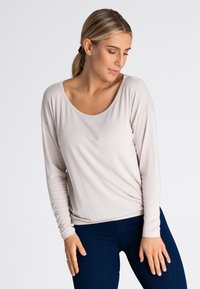 Jasnobeżowa bluzka z długim rękawem i szerokim dekoltem w kształcie litery U, luźny krój i teksturowana tkanina, w połączeniu z ciemnoniebieskimi dżinsami.