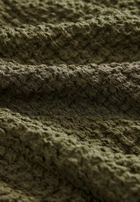 Mīksts audums dziļā olīvzaļā krāsā ar viļņotu rakstu un paaugstinātu struktūru, kas piedāvā vizuālu un taustāmu interesi.