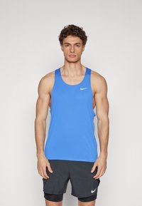 Top atlético azul de tela texturizada, con un escote amplio y el logo de Nike en el pecho. Combinado con pantalones cortos negros.