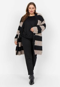 Raitane cardigan vaaleanbeigessä ja mustassa, tekstuurinen kangas, avonainen etuosa, löysä malli, pitkät hihat, yhdistetty mustan yläosan ja housujen kanssa.