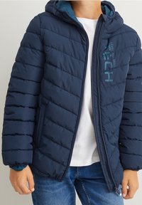 Granatowa, pikowana kurtka z ociepleniem, z dołączonym kapturem i zamkiem błyskawicznym z przodu. Posiada detal z napisem "TECH" na lewej piersi.