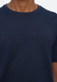 Marineblå bomull T-skjorte med et preget "MICHAEL KORS"-logo på forsiden. Klassisk rund hals og kortermet. Glatt tekstur.