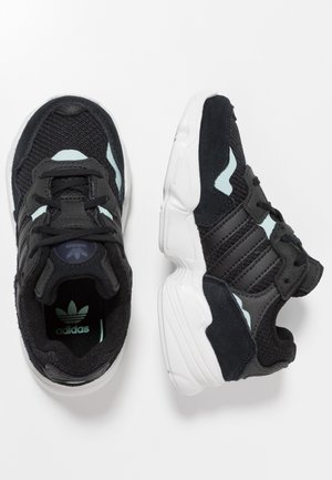 Schwarze Sportschuhe mit einem Obermaterial aus Mesh und Wildleder, weißer Zwischensohle und hellblauen Akzenten sowie einer strukturierten Gummilaufsohle.