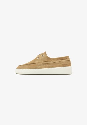 Chaussure décontractée en daim marron clair avec semelle blanche épaisse, lacets à l'avant et détails de couture subtils sur fond blanc uni.