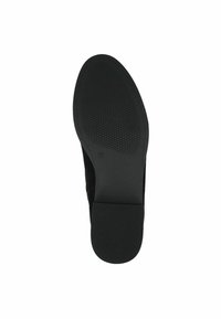 Zapato negro de suela plana con una suela de goma texturizada. Presenta una parte superior suave y un tacón bajo para estabilidad. Diseño limpio y minimalista.