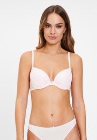 Lichte roze bh met gevoerde cups, verstelbare bandjes en een klein strikdetail in het midden. Glad textuur en een ondersteunend, modern ontwerp.