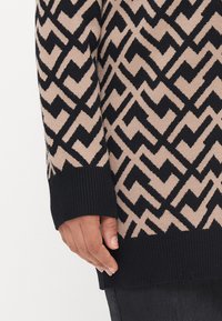 Knitted sweater featuring a geometric zigzag pattern in black and beige. Ribbed cuffs and hem with a soft texture; long sleeves.