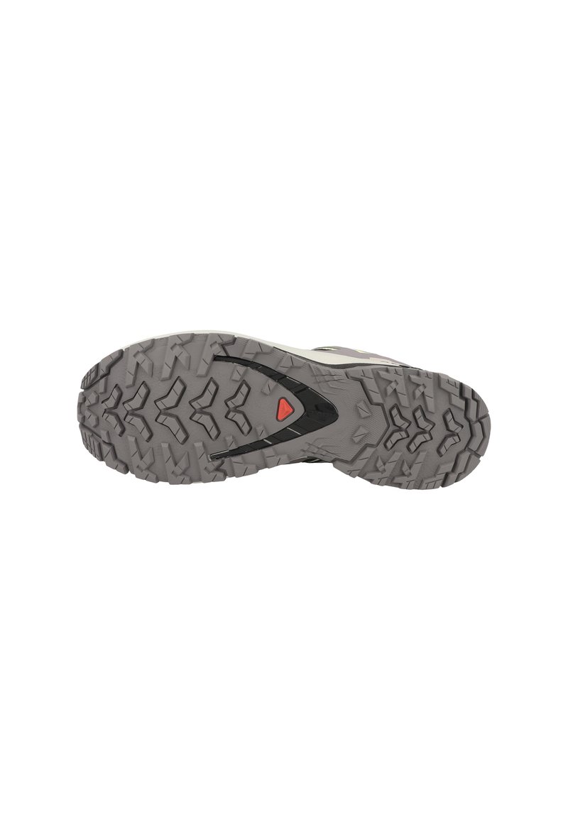 La suola della scarpa presenta un materiale in gomma texturizzato di colore grigio. Il motivo del battistrada include tasselli multidirezionali per una migliore trazione. Dettaglio accentato in rosso presente.