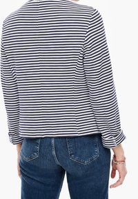 Veste rayée bleu marine et blanche, présentant une coupe droite, des manches longues et un ourlet bas. Portée avec un jean en denim foncé, montrant un design simple.