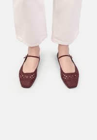 Balerini împletiți în nuanța burgundă, cu un design cu vârf pătrat, dotate cu o curea pentru gleznă și modele deschise. Materialul pare a fi texturat și respirabil.