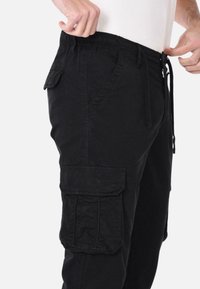 Pantaloni cargo neri realizzati in tessuto misto cotone, con vita elastica, cordino, tasche laterali e una tasca cargo sulla coscia.