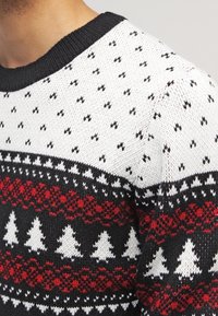 Svart, vit och röd stickad tröja med ett mönster av träd och geometriska former. Ribbad halsringning, textilier med struktur.