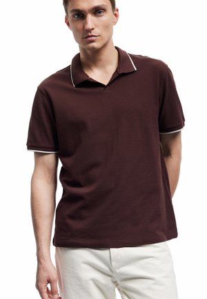 Polo burgundy avec une texture douce, présentant un col et des accents d'ourlet blancs contrastants, associé à un pantalon clair.