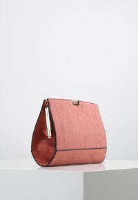 Roze suède handtas met een gladde textuur, unieke taps toelopende vorm en zwarte accentstiksels. Voorzien van een metalen sluiting en een handvat.