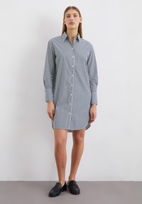 Knoopjurk in marineblauw en witte verticale strepen, met lange mouwen, een kraag en een ontspannen pasvorm, die boven de knie eindigt.