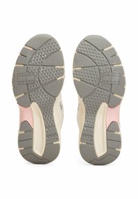 Semelles de baskets grises avec des motifs de traction en caoutchouc et étiquetées "TOMMY JEANS". Présentent des accents beiges et une section rose au niveau du talon.
