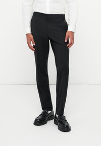Schwarze maßgeschneiderte Hose mit glatter Textur und schmaler Passform, mit flachem Bund und seitlichen Taschen, kombiniert mit polierten schwarzen Schuhen.