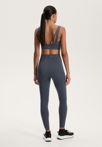 Sportbehå och leggingsset i mörkgrått, med en design med strappy rygg, slät textur och figurnära passform. Svarta sneakers fulländar looken.