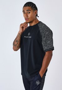 Camiseta negra con mangas con patrón, que presenta un logotipo y el texto "PROJECT X PARIS". La tela parece suave; las mangas tienen un diseño geométrico.