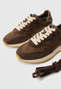 Καφέ σουέτ αθλητικά παπούτσια με γεωμετρικό μοτίβο, μπεζ κο ρδόνια και κρεμ σόλα από καουτσούκ. Περιλαμβάνει ένα επιπλέον καφέ κορδόνι.