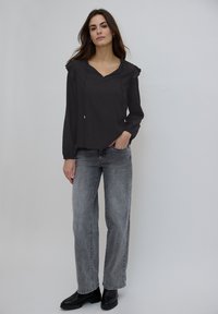 Haut noir à manches longues avec un col en V et des épaules à volants, associé à un jean gris à jambes larges et des bottines noires. Tissu lisse, coupe décontractée.