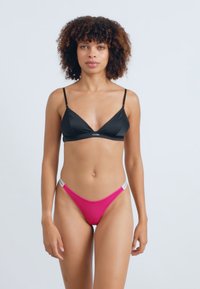 Haut de bikini triangulaire noir avec des fines bretelles, associé à un bas de bikini rose à taille haute avec des accents argentés. Texture lisse dans l'ensemble.