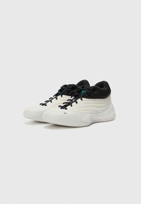 Scarpe sportive bianche e nere con un design strutturato, dotate di una parte superiore liscia, lacci neri e una suola con motivo.