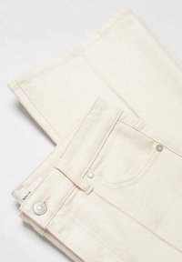 Jean en denim beige plié avec coutures visibles, poches latérales et boutons en métal argenté. Texture lisse et design simple.