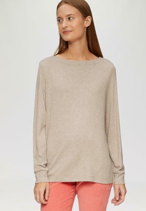 Beige Langarmshirt mit weit ausgeschnittenem Hals, weichem Stoff und lässigem Schnitt, kombiniert mit leuchtend korallenfarbenen Hosen.