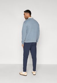 Ανοιχτό μπλε φούτερ με ορατό γιακά, σε συνδυασμό με σκούρο μπλε παντελόνι. Το σύνολο έχει χαλαρή εφαρμογή και τα παπούτσια είναι σε αποχρώσεις κρεμ και μπεζ.