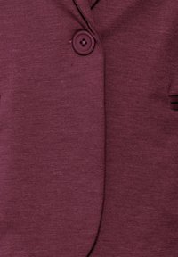 Kadar blizu maroon tkanine s teksturom, na odjeći sa jednim okruglim dugmetom pričvršćenim blizu ovratnika.