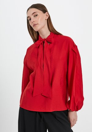 Red blouse with a tied neckline, long puff sleeves, and a relaxed fit. Made from lightweight fabric with a slightly crinkled texture.