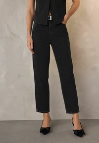 Mustat denim-suorat lahkeet farkut korkealla vyötäröllä, joissa on hienovarainen haalistunut rakenne ja etutaskut, yhdistettynä mustiin jalkineisiin, joissa on sukkia.