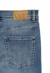 Jeans z denimu v světle modré barvě, s koženým štítkem na pase s označením "VMD" a jednou zadní kapsou s prošitými detaily.