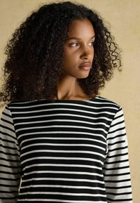 Triibuline pikkade varrukatega top, millel on mustad ja valged horisontaalsed triibud, lai kaelus ning pehme kangas sujuva tekstuuriga.