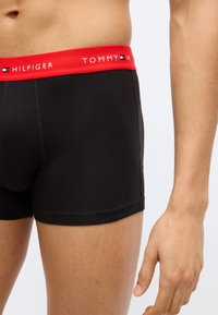 Μαύρα βαμβακερά μπόξερ με κόκκινη ελαστική μέση που φέρει το κείμενο «TOMMY HILFIGER» και ένα λογότυπο. Τακτικές ραφές και εφαρμοστή σχεδίαση.
