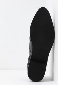 Chaussure en cuir noir avec un motif perforé complexe. Bout pointu et semelle plate en caoutchouc. Taille 39 indiquée sous la chaussure.
