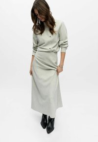 Ensemble gris clair deux pièces comprenant un haut boutonné à manches longues et une jupe longue jusqu'au sol. Porté avec des bottines noires.