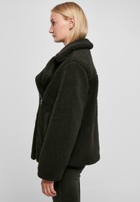 Zwarte fleecejack met een brede kraag, ontspannen pasvorm en ritssluiting. Het gestructureerde materiaal heeft een zachte, pluche uitstraling.