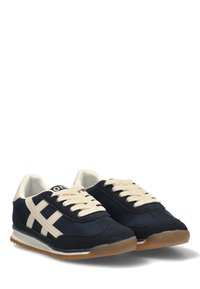 Zapatillas azul marino con cordones y detalles en crema. Presentan un revestimiento de ante, suela de goma y tres franjas en el costado. Diseño casual.