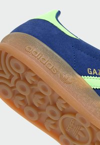 Semelle de chaussure Adidas Gazelle bleue et vert néon avec motif de bande de roulement circulaire et semelle extérieure en caoutchouc translucide visible.
