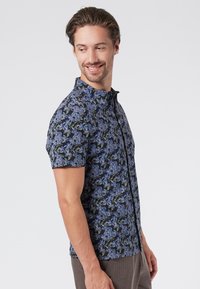 Camisa de manga corta con fondo azul marino y un patrón de flores en tonos de azul y verde. Cuello abotonado y diseño ajustado.